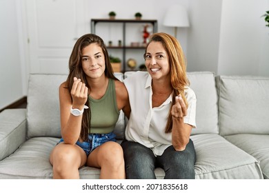 Mother And Daughter Together Sitting On The Sofa At Home Doing Money Gesture With Hands, Asking For Salary Payment, Millionaire Business 