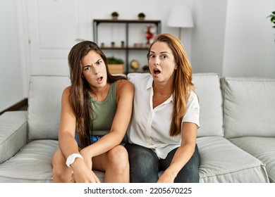 Mother And Daughter Together Sitting On The Sofa At Home In Shock Face, Looking Skeptical And Sarcastic, Surprised With Open Mouth 