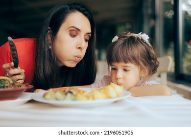 
Mother And Daughter Trying To Cool Off A Restaurant Meal Dish
Mom And Her Little Girl Making A Teamwork Effort To Blow In The Hot Plate Of Food 
