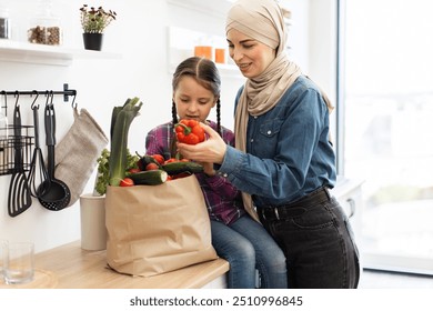 Mother and daughter unpacking fresh groceries in kitchen with paper bag filled with vegetables. Family enjoying time cooking healthy meal together in cozy home. - Powered by Shutterstock