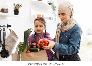 Mother and daughter unpacking groceries in bright kitchen. Child and parent smiling while organizing fresh vegetables. Family bonding while preparing healthy meal. - Powered by Shutterstock