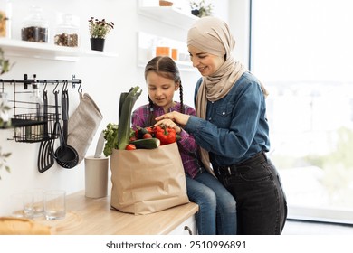 Mother and daughter unpacking groceries in modern kitchen. They are smiling and enjoying time together. Fresh vegetables are in grocery bag on countertop. - Powered by Shutterstock