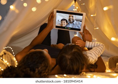 Mother and daughter using digital tablet while lying in kid tent doing a video call with father and son. Indian family in online conversation with each other during quarantine and social distancing. - Powered by Shutterstock