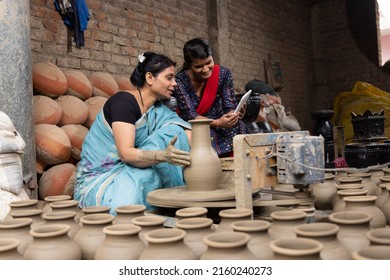 Mother and daughter using digital tablet while making clay pot on spinning wheel at village - Powered by Shutterstock