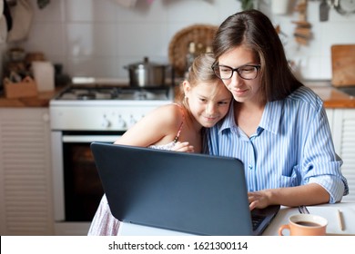 Mother And Daughter Using Laptop And Internet. Freelancer Workplace In Cozy Kitchen. Woman And Child Girl Together. Concept Of Female Business, Working Mom, Freelance, Home Office. Lifestyle Moment.