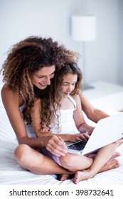 Mother And Daughter Using Laptop On Bed In Bedroom