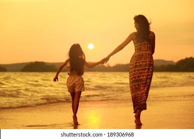 Mother And Daughter Walking On The Beach With Sunset