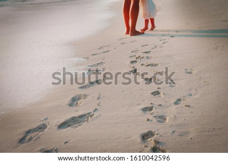 mother and daughter walking on beach leaving footprint in sand