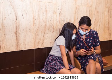 Mother And Daughter Watching Smart Phone And Wearing Face Mask On The Subway Station.