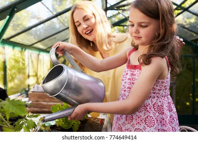 Mother And Daughter Watering Hanging Basket In Greenhouse