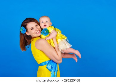 Mother And Daughter Wearing The Same Yellow Dress. Happy Mother Holding Her Daughter In Her Arms. The Concept Of A Happy Family.