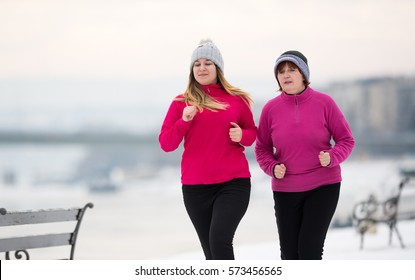 Mother and daughter wearing sportswear and running on snow during winter time