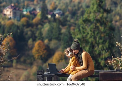 Mother And Daughter Work On Laptop Outside On Terrace In Autumn.