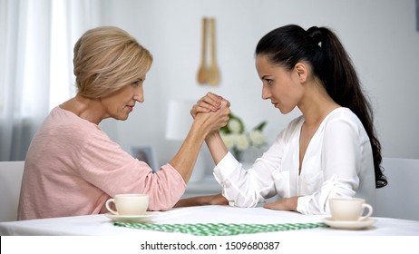 Mother and daughter-in-law looking on each other during arm wrestling battle