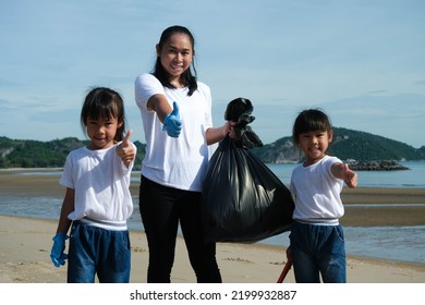 Mother And Daughters In Gloves Cleaning Up The Beach. Group Of Young Volunteers Helping To Keep Nature Clean And Picking Up The Garbage From A Sandy Shore. Earth Day Concept