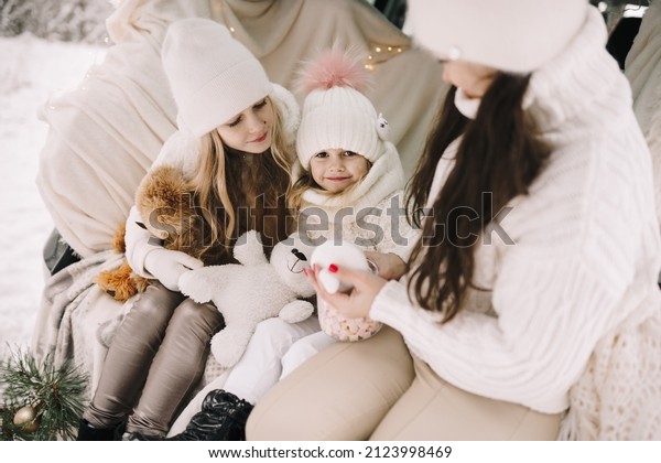 Mother and daughters. Mom and daughters drink\
hot chocolate in the car. Family trip in the winter forest. \
Christmas holiday in the\
mountains.