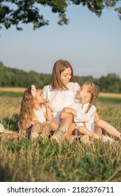 Mother and daughters relax in nature. Vertical photo of a mother with children. Family photo shoot in the village in the field. Psychology of the relationship between mother and child
