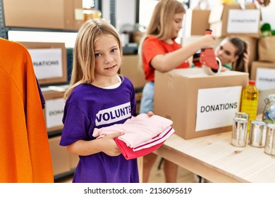 Mother and daughters wearing volunteer uniform holding folded clothes working at charity center