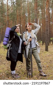 Mother And Dauhter Have Lost In Wood Standing In Middle Of Forest Discussing Searching For Destination. Elderly Woman And Offspring Wearing Hicking Shoes Holding Hicking Equipment Girl Talks To