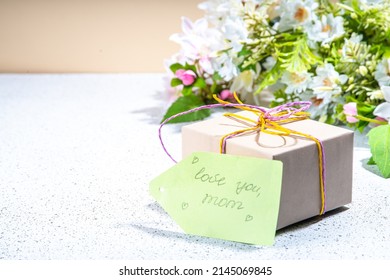 Mother Day Greeting Card Background With Present And Flowers. Gift Box With Festive Ribbon, Tag Love You Mom, Spring Bloom Flowering Branches Bouquet Flatlay Copy Space