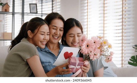 Mother day two grown up child cuddle hug give flower gift box red heart card to mature mum. Love kiss care mom asia middle age adult three people sitting at home sofa happy smile enjoy family time. - Powered by Shutterstock