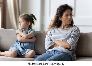 Mother disobedient daughter sit apart on sofa with arms crossed posture of discontent, think feels frustrated. Challenges of kids raising, lack of emotional bonding, child-rearing difficulties concept