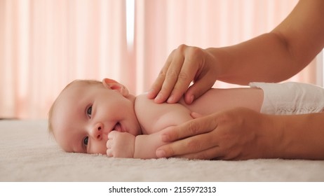 Mother doing massage on her healthy infant baby. Small caucasian newborn laying on his belly while his mother is performing a massage for his small back and developing muscles. 