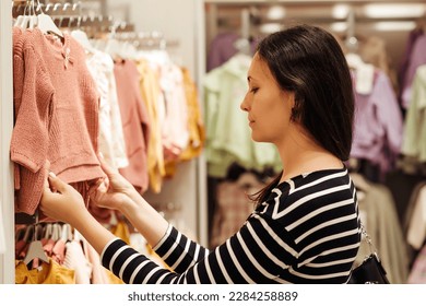 Mother doing shopping in baby shop. Baby fashion, shopping time, sale and pregnancy concept. Pregnant woman chooses clothes for her future daughter. - Powered by Shutterstock