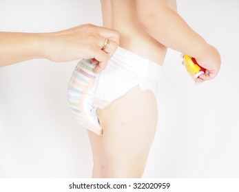 Mother Dressing Up Toddler In Diaper While Standing, Holding A Yellow And Red Toy Car