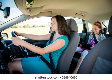 Mother Driving Car And Child Sitting On Back Seat And Playing With Tablet