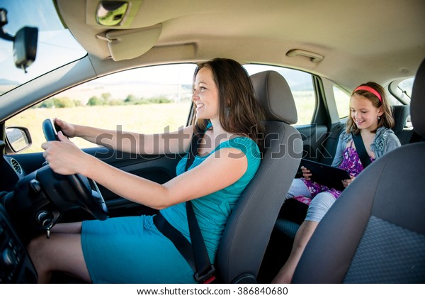 Mother driving car and child sitting on back seat\
and playing with tablet