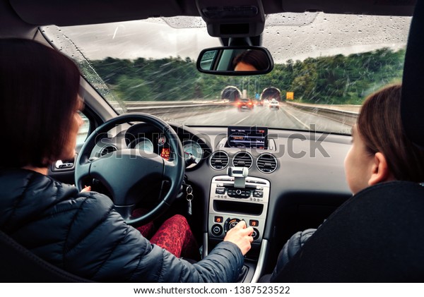 Mother driving daughter in the passenger seat\
on the busy highway on the rainy\
day