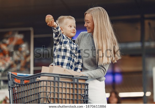Mother is driving in a trolley. Family in a\
parking near a\
supermarket.