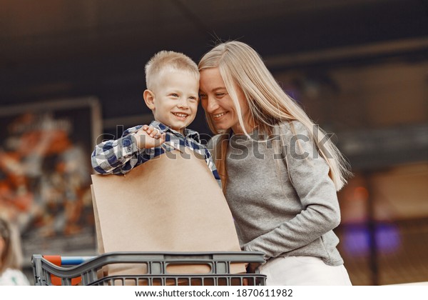 Mother is driving in a trolley. Family in a\
parking near a\
supermarket.
