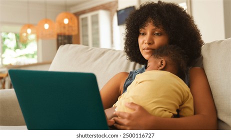 A mother engages with her laptop while caring for her sleeping baby. - Powered by Shutterstock