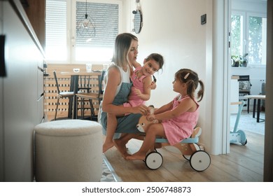 A mother engages in playful interaction with her children as they ride a toy tricycle inside their modern home, capturing a moment of joy and family bonding. - Powered by Shutterstock