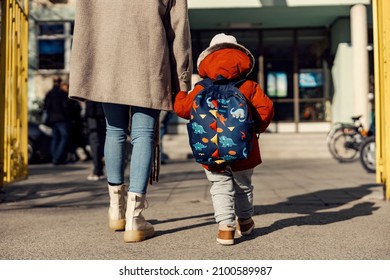 A mother entering the kindergarten yard with her preschooler boy.