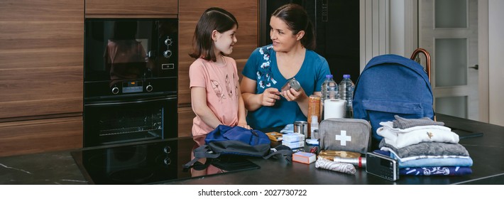 Mother explaining to her daughter how to prepare an emergency backpack in the kitchen