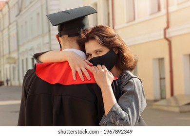 Mother In Face Mask Hugs Her Son Student In Graduation Gown And A Square Cap After Ceremony. Class 2021