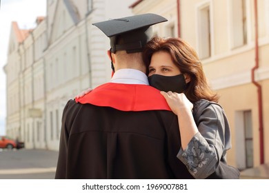 Mother In Face Mask Hugs Her Son Student In Graduation Gown And A Square Cap After Ceremony. Class 2021