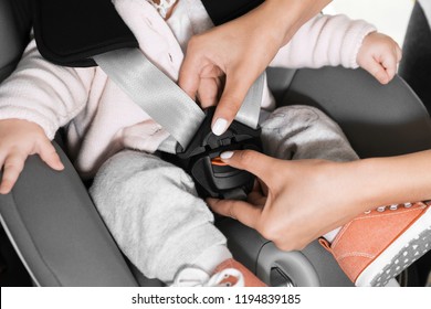 Mother fastening baby to child safety seat inside car