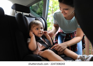 Mother fastening her daughter in child safety seat inside car - Powered by Shutterstock