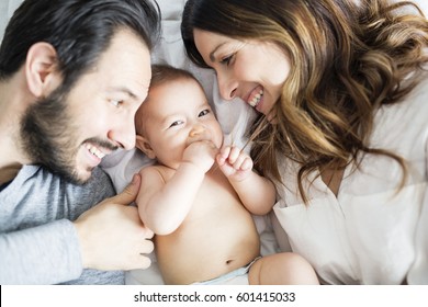 A Mother Father And Baby Child On A White Bed.