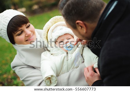 Mother and father with baby dressed in warm clothes walking on a sunny day outdoors. Happy family spend time together.