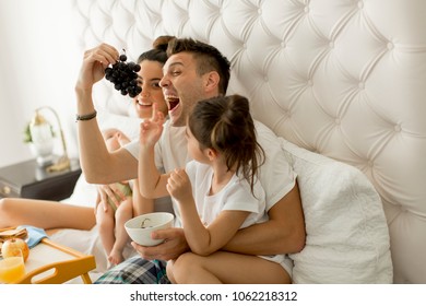 Mother, Father, Baby And Little Girl On The Bed Eating Grapes