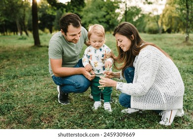 Mother, father, child catch soap bubbles on green grass in park enjoying sunny summer day. Family blows soap bubbles. Toddler little cute son, dad, mom walking and playing in spring garden. Closeup. - Powered by Shutterstock