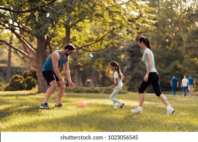 Mother father and daughter play football with a red soccer ball. They play in the park - Powered by Shutterstock