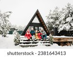 Mother, father, daughter and sons spend winter holidays at cottage. Company people childs celebrate New Year. Big family with kids have fun on terrace of mountain country house in snow forest together