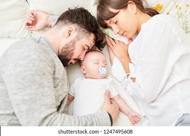 Mother And Father As Happy Parents Sleep Next To Their Little Baby