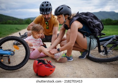 Mother and father helping their little daughter after falling off bicycle outdoors - Powered by Shutterstock